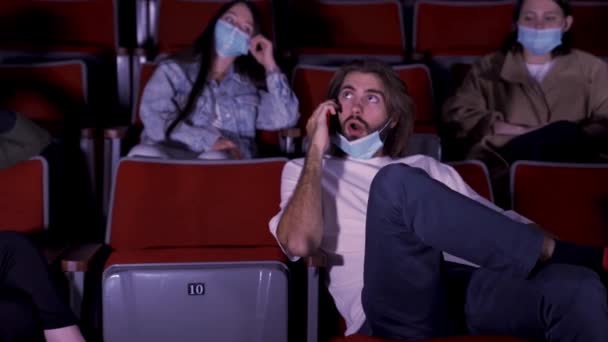 Sebevědomý mladý muž mluví v kině na mobilním telefonu, diváci vypadají naštvaně. Média. Mladý muž mluví nahlas na smartphone při sledování filmu v kině a znepokojující publikum. — Stock video