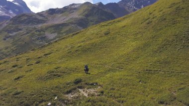 Yeşil bir dağ yamacında ata binen bir adamın hava manzarası. Şarjör. Güzel bir yaz günü, dağ sıraları, bulutlu gökyüzü ve tepeyi kaplayan yeşil çimenler..