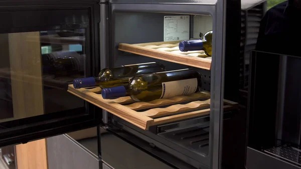 Бутылки вина охлаждаются на деревянных полках холодильника. Бытовая утварь. Закрывая домашний холодильник, человек открывает дверь холодильной машины. — стоковое фото