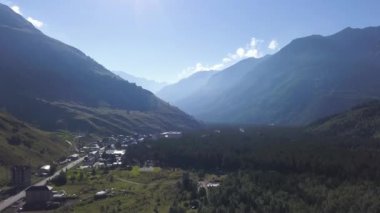 Dağlar arasında bir vadide bulunan Gürcistan köyünün havacılığı. Şarjör. Bir yol ve mavi gökyüzü arka planında evleri olan Kafkas dağları vadisi..