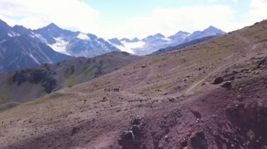 Dağ yamaçlarının havadan görünüşü ve yürüyüş yapan insanlar. Şarjör. Bir grup turist, arka planda karlı dağ zirveleri olan dev bir kayanın yamacında seyahat ediyor..
