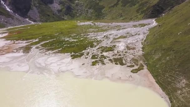 Bergsee von beiger oder milchiger Farbe in einem Tal. Clip. Luftaufnahme eines ungewöhnlichen weißen Sees in der Nähe des grünen Feldes am Fuße der Berge an einem sonnigen Sommertag. — Stockvideo