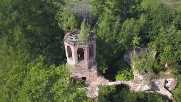 Luftaufnahme von üppigem Wald an einem sonnigen Sommertag und einer alten Kirche. Clip. Überfliegen der Ruinen der alten steinernen Kirche inmitten grüner Bäume. — Stockvideo