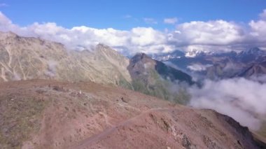Mavi gökyüzü arka planında bulutlu bir dağ sırası. Şarjör. Dağ zirvesinden, sonsuz yüksek tepelere, beyaz akan bulutlara, doğanın güzelliğine bak..