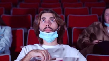 Karantinada sinema, adam film izliyor ve patlamış mısır yiyor. Medya. Coronavirus salgını güvenlik kuralları, koruyucu yüz maskeli bir adam bir sıra oditoryumda oturuyor, boş zaman, gençlik kültürü kavramı.