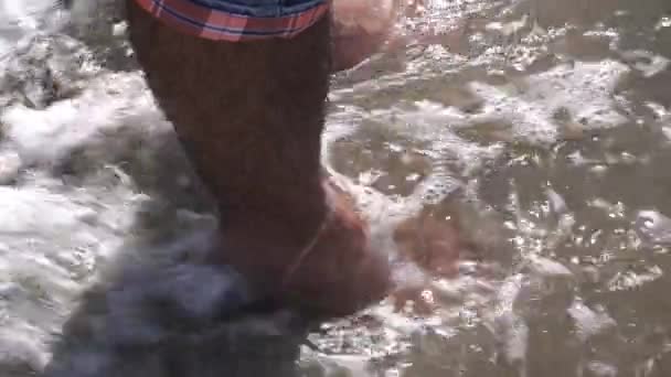 바위와 수컷의 발을 덮고 있는 돌 해변에 파도가 일고 있다. 미디어. 해변에서 서, 여름 휴식과 공터 개념에 서 사람의 닫기. — 비디오