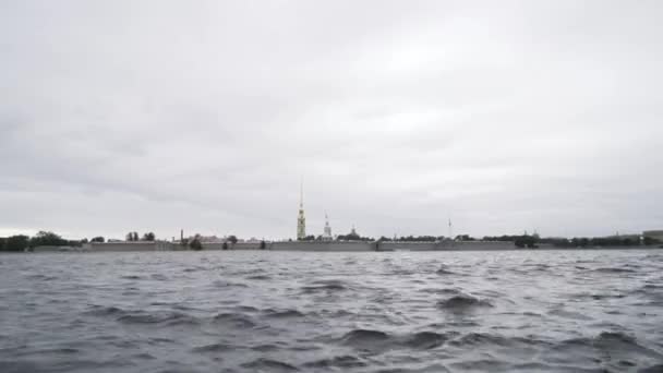 Fortaleza Petropavlovskaya y el río Neva. Acción. San Petersburgo, Rusia, primer plano de la superficie ondulada del agua de un río y la fortaleza lejos en la distancia sobre el fondo nublado del cielo. — Vídeos de Stock