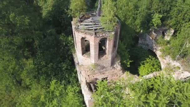 Flygfoto över lummig skog en solig sommardag och en gammal kyrka. Klipp. Flygande över ruiner av den gamla steniga kyrkan som ligger bland gröna träd. — Stockvideo