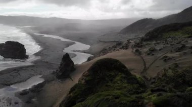 Kara kum ve Tazman Denizi 'nin olduğu sahili. Bulutlu gökyüzünün altında, vahşi batı sahillerinde.