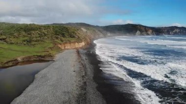 Nefes kesen kıyı manzarası, siyah kumsalın yeşil tepelerle buluşmasını gösteriyor.