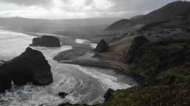 Okyanus dalgaları, bulutlu bir günde İzlanda 'daki Reynisfjara kara kumsalına çarpıyor.