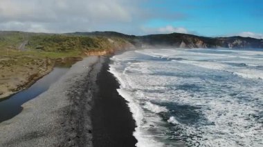 Okyanus dalgaları denize dökülen bir nehrin yanındaki siyah kumsala çarpıyor.