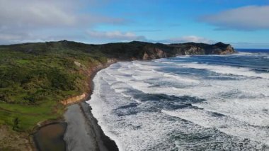 Siyah kum, dramatik uçurumlar ve güçlü okyanus dalgalarıyla nefes kesici Whatipu sahili manzarası.