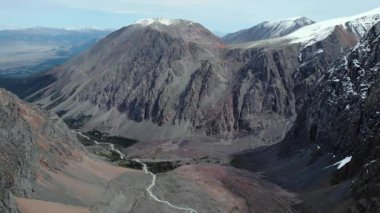 Karla kaplı tepeleri ve aşağıdaki vadiden akan dolambaçlı bir nehri olan görkemli bir dağ silsilesinin nefes kesici manzarası. Medya