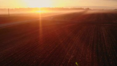 Güzel, sisli bir gündoğumu sırasında bir kır yolunun havadan görünüşü ve arabalarla tarlaları sürmek. Medya