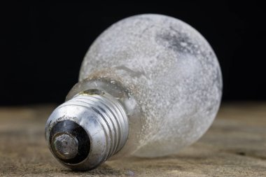 Tahta bir masanın üzerinde yatan ampul. Eski bağlamada aydınlatma aksesuarları. Koyu arka plan.