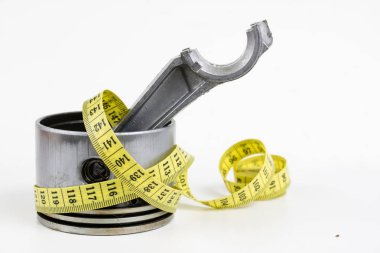 Bir piston bir içten yanmalı motor ve bir terzi ölçü birimi üzerinde beyaz bir tablo. Araba parçaları ve terzi santimetre. Beyaz arka plan.