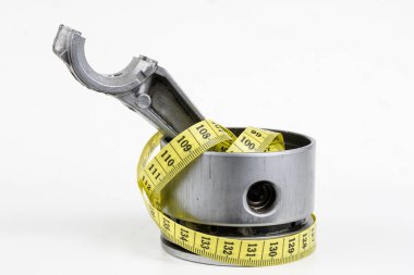 Bir piston bir içten yanmalı motor ve bir terzi ölçü birimi üzerinde beyaz bir tablo. Araba parçaları ve terzi santimetre. Beyaz arka plan.