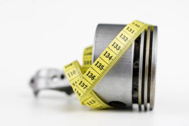 Bir piston bir içten yanmalı motor ve bir terzi ölçü birimi üzerinde beyaz bir tablo. Araba parçaları ve terzi santimetre. Beyaz arka plan.