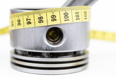 Bir piston bir içten yanmalı motor ve bir terzi ölçü birimi üzerinde beyaz bir tablo. Araba parçaları ve terzi santimetre. Beyaz arka plan.