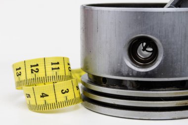 Bir piston bir içten yanmalı motor ve bir terzi ölçü birimi üzerinde beyaz bir tablo. Araba parçaları ve terzi santimetre. Beyaz arka plan.