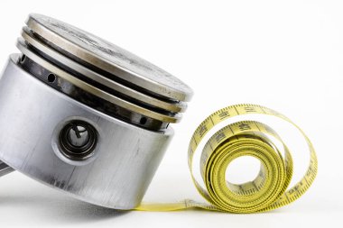 Bir piston bir içten yanmalı motor ve bir terzi ölçü birimi üzerinde beyaz bir tablo. Araba parçaları ve terzi santimetre. Beyaz arka plan.