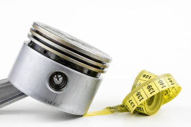 Bir piston bir içten yanmalı motor ve bir terzi ölçü birimi üzerinde beyaz bir tablo. Araba parçaları ve terzi santimetre. Beyaz arka plan.