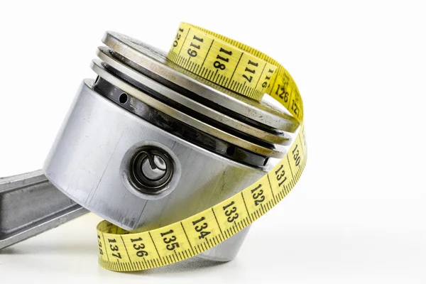 Bir piston bir içten yanmalı motor ve bir terzi ölçü birimi üzerinde beyaz bir tablo. Araba parçaları ve terzi santimetre. Beyaz arka plan.