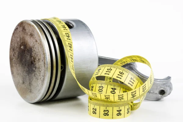 Bir piston bir içten yanmalı motor ve bir terzi ölçü birimi üzerinde beyaz bir tablo. Araba parçaları ve terzi santimetre. Beyaz arka plan.