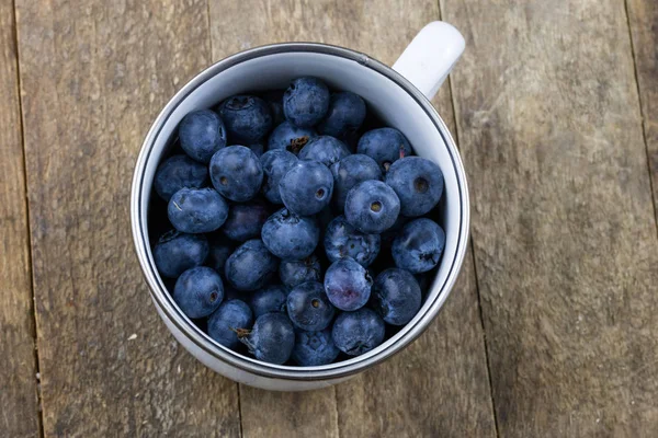 Olgun yaban mersini meyve ahşap mutfak masasında kapsayıcı. Meyve tatlı için hazır. Koyu arka plan.