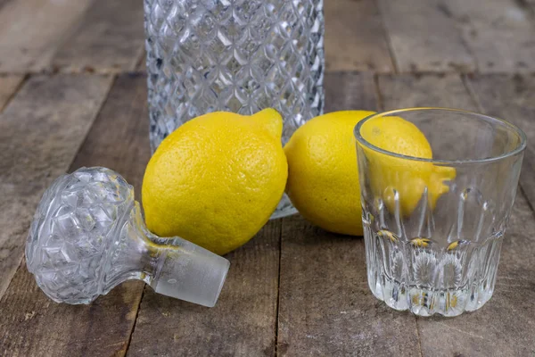 Glass container of cold water with lemon on an old wooden table. Cool drinks on a hot day. Dark background.