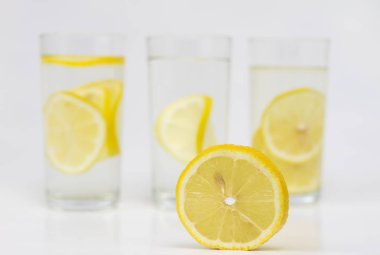 Bir bardak soğuk su beyaz mutfak masası üzerinde limonlu. Sıcak havalarda serinletici bir içki. Açık renkli.