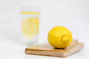 Bir bardak soğuk su beyaz mutfak masası üzerinde limonlu. Sıcak havalarda serinletici bir içki. Açık renkli.