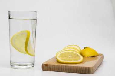 Bir bardak soğuk su beyaz mutfak masası üzerinde limonlu. Sıcak havalarda serinletici bir içki. Açık renkli.