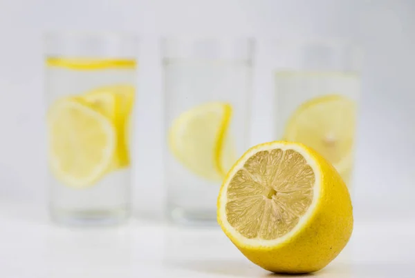 A glass of cold water with lemon on a white kitchen table. A refreshing drink in warm weather. Light background.
