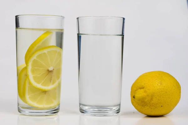 A glass of cold water with lemon on a white kitchen table. A refreshing drink in warm weather. Light background.