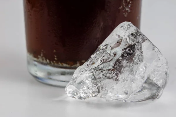 Cold drink with ice in a glass on a white table. A way to cool down on hot days. White background.