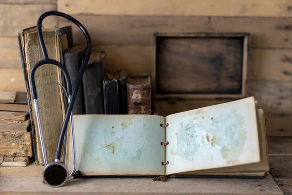 Stethoscope and a case on an old desk. Medical magazines and medical accessories on a wooden table. Dark background.