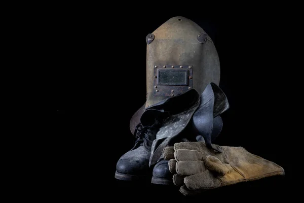 An old mask a protective suit for a welder. Occupational health and safety clothing for production workers on a workshop table. Black background.