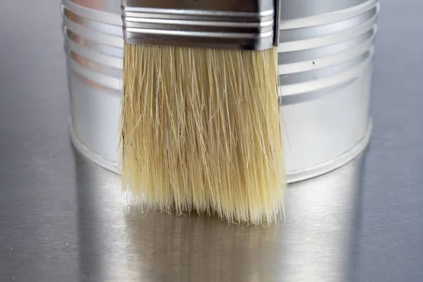 A paint brush and a can of paint on a workshop table. Painting accessories for construction workers. Light background.