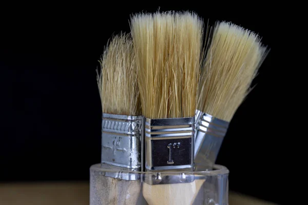 A brush for simple housework and a can of paint. Repair accessories on a metal table. Dark background.
