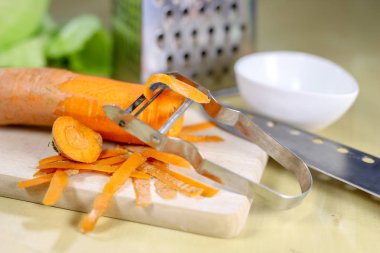 Bir metal mutfak rendeleyin taze havuç rendesi. Mutfak masasının üzerinde bir yemekle salata için hazırlanan sebzeler. Açık renkli.