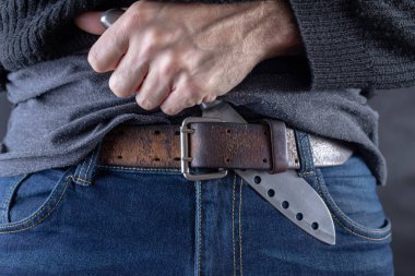 Keskin çelik bıçak kot pantolon arka planı elinde tuttu. Bir suikastçı elinde tehlikeli zehir. Koyu arka plan.