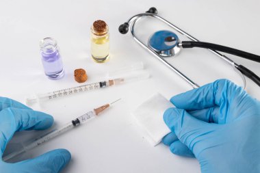 Küçük bir şırınga, tıp ve doktorun elinde eldiven. Mutfak eşyaları klinikte tedavi için gerekli. Açık renkli.
