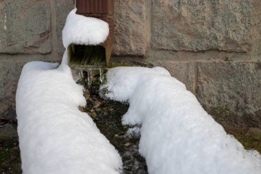 Tek ailelik bir binada karla kaplı bir oluk. Çatıdan su akı. Sezon kış.