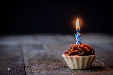 Bir mum bir ahşap mutfak masasında Cupcake tatma. Koyu arka plan.