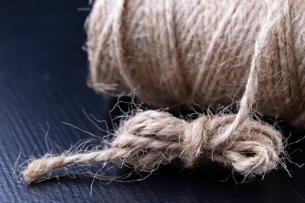 Twine for wrapping packages on the table. Jute string wrapped around the roller. Dark background.