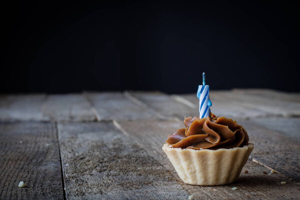 Дегустация кекса со свечой на деревянном кухонном столе. Темный фон
.