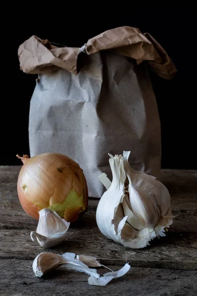 Onions and garlic in a paper bag. Wooden dark table.
