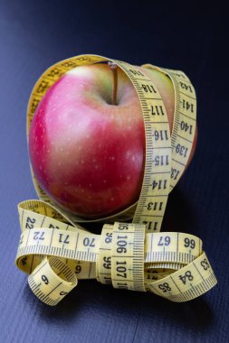 Lezzetli, Olgun elma bir ölçüm bandı sarılmış. Meyve karanlık bir tablo. Siyah arka plan.